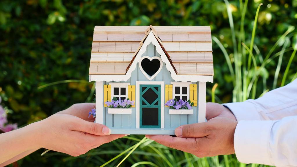 A hand holding a little wooden house with a heart on the roof