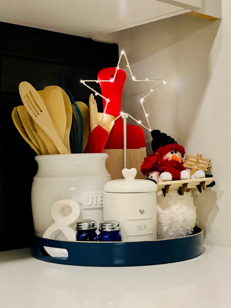 A brightl blue round tray with a white utinsel holders, a sugar jar, blue salt and pepper shakers, and bright red cutting board.  